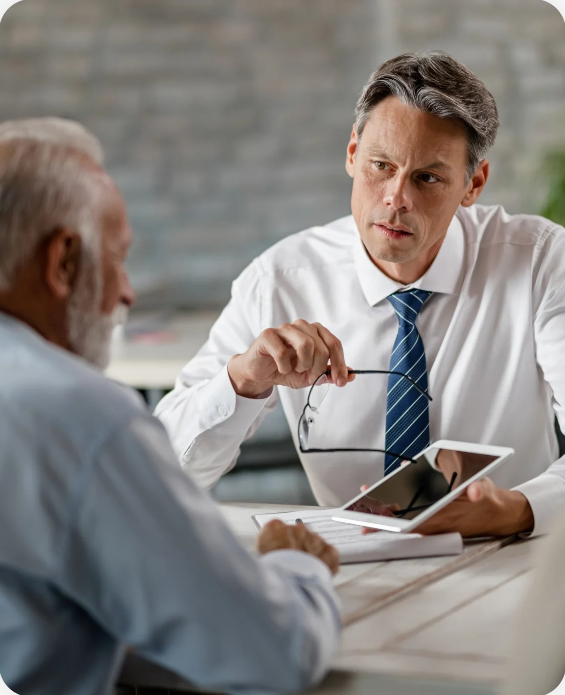 Insurance agent communicating with senior clients while showing something touchpad meeting office@2x